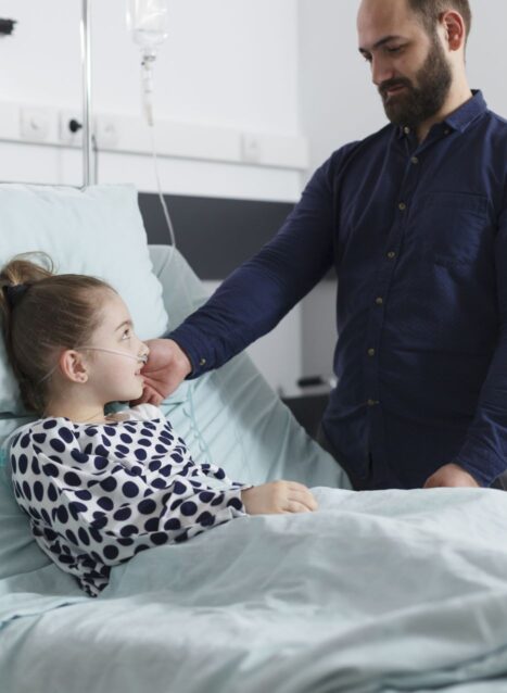 il-padre-attento-e-solidale-accarezza-la-piccola-figlia-malata-mentre-giace-nel-letto-del-paziente-dell-ospedale